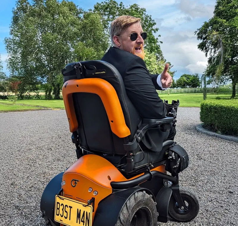 A man in a suit using a powerchair on gravel