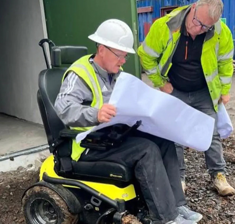 A man in a high vis vest doing work in a powerchair
